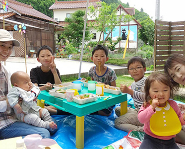女性と子どもたちで外でお弁当を食べている